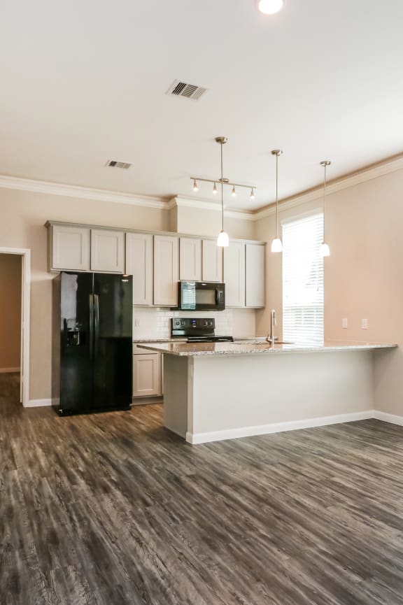 an empty living room with a kitchen in the background