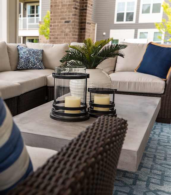 A patio with a couch, pillows, and a lantern.
