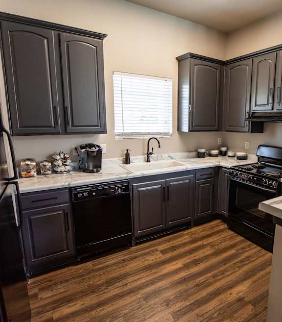 A kitchen with black cabinets and a wooden floor.