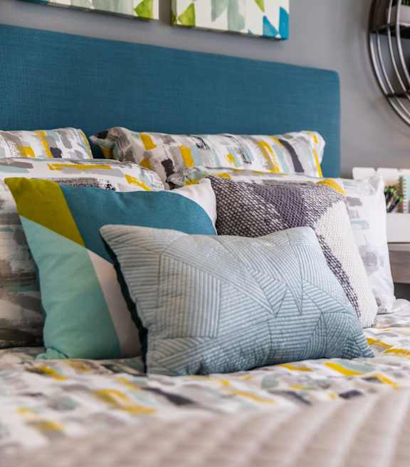 A bed with a blue headboard and a white bedspread with yellow and blue pillows.