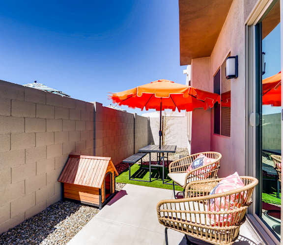 A patio with a red umbrella and wicker chairs.