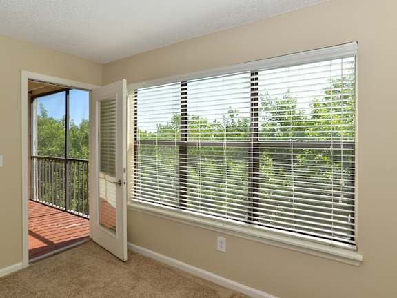 A room with a window covered by white blinds and a door leading to a deck.
