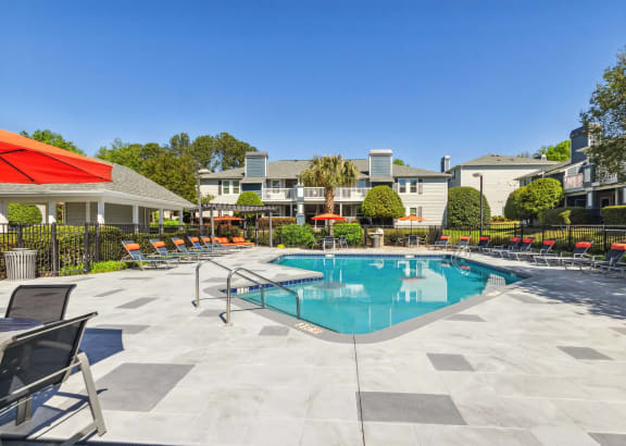 a swimming pool with chairs and umbrellas and apartments in the background