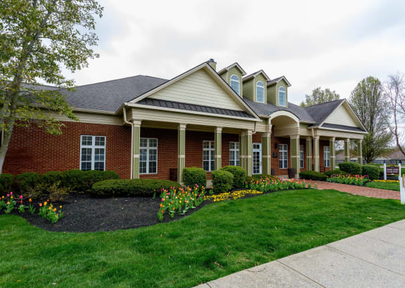 the front of a brick house with a lawn and flowers