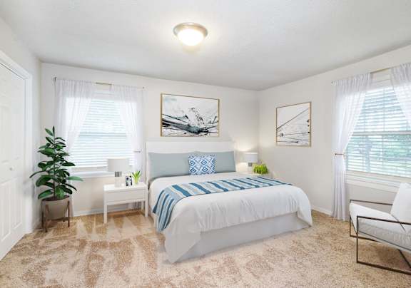 A bedroom with a bed, chair, and potted plant.