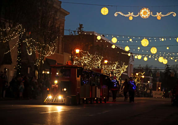 a trolley car driving down a street at night with christmas lights