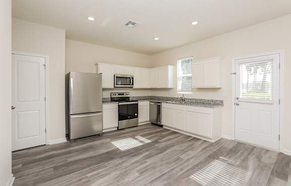 A kitchen with a refrigerator, microwave, oven, and sink.