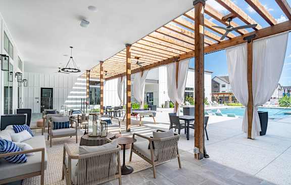 A patio with a white ceiling and a pool in the background.