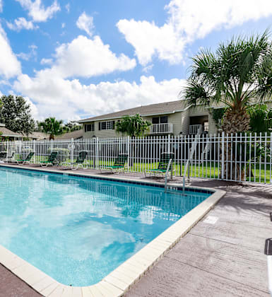 A large outdoor swimming pool surrounded by a fence and lounge chairs.
