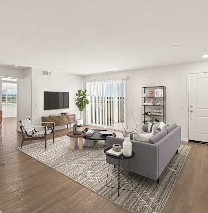 A modern living room with a grey sofa, wooden floors, and a white kitchen area.
