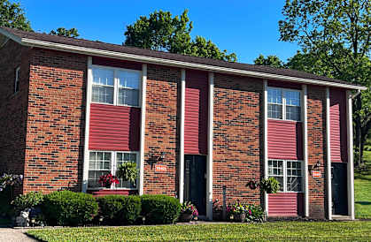 A red brick house with a red door and a green lawn.