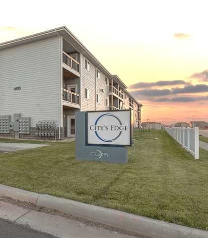 City’s Edge apartment exterior with sign and sunset view