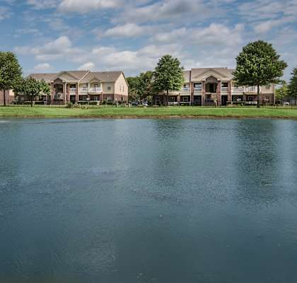 A fountain in the middle of a lake in front of apartment buildings.