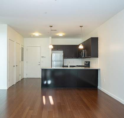 an empty living room and kitchen with wood flooring and white walls