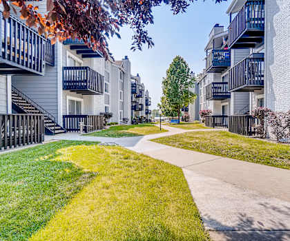 A row of apartment buildings with a sidewalk and green grass.