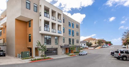 A modern apartment building with a parking lot in front.