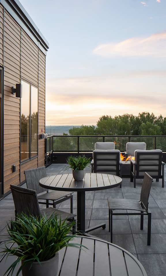 A balcony with a table and chairs overlooking a cityscape at dusk.