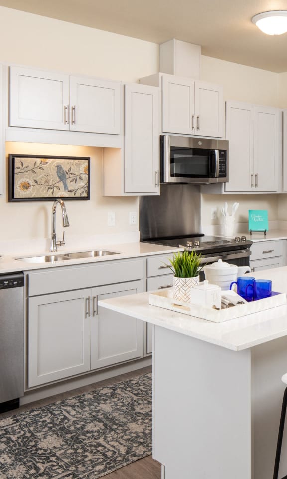 a white kitchen with stainless steel appliances and a white island with white chairs