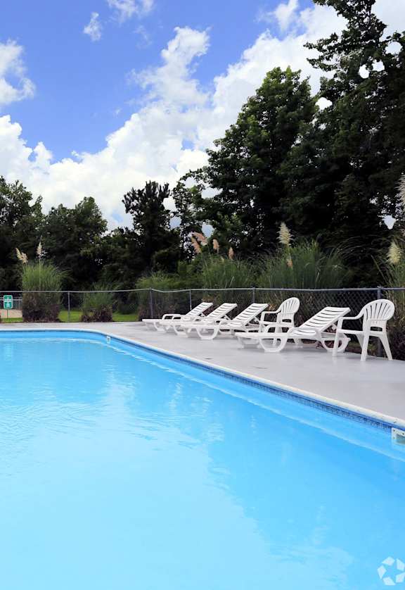 a swimming pool with white chairs and a fence around it