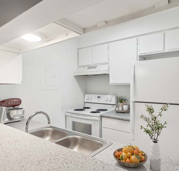 A kitchen with white appliances and a bowl of fruit on the counter.