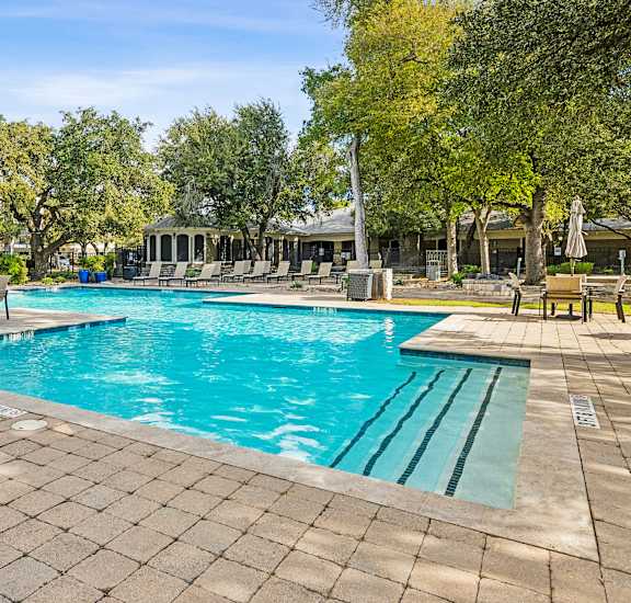 A large outdoor swimming pool surrounded by trees and lounge chairs.