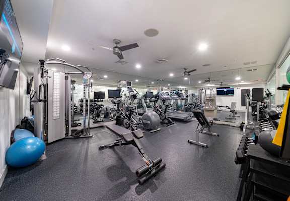 a gym with weights and cardio equipment on the floor and a ceiling fan