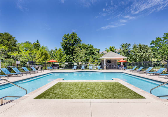 A large swimming pool surrounded by lawn chairs and trees.