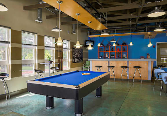A pool table is in the middle of a room with a bar and stools.