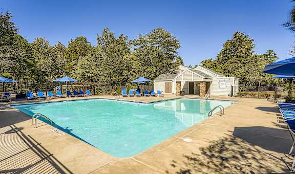 A large swimming pool surrounded by trees and a house in the background.