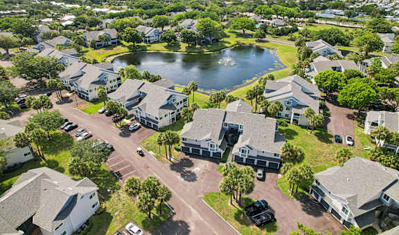 A bird's eye view of a residential area with houses, a lake, and a parking lot at The Villages Apartment of Bayan Grove in Boynton Beach, FL