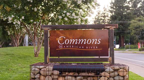 A sign that says "Commons @ American River" is displayed on a stone wall.