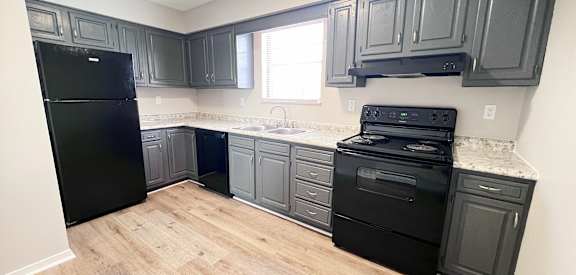 A kitchen with black appliances and wooden floors.