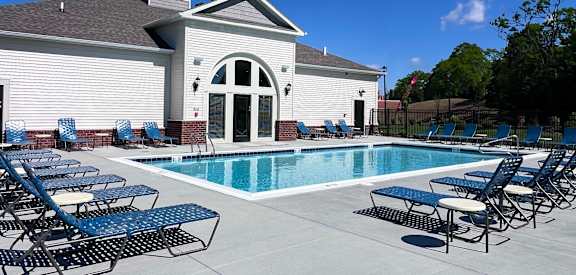 A pool with chairs around it and a building behind it.