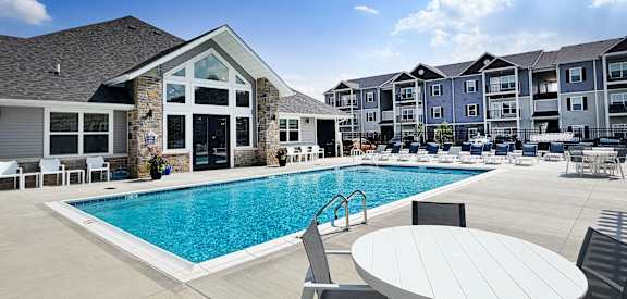 A swimming pool is surrounded by chairs and tables in front of a building.