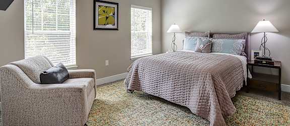 A bedroom with a bed, chair, and lamp.
