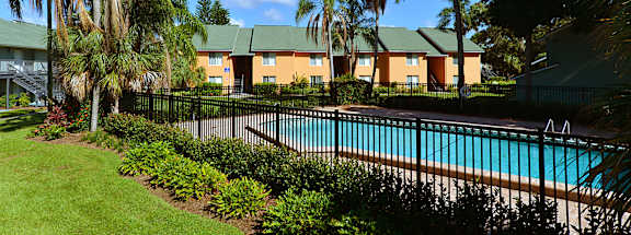 A pool surrounded by greenery and trees with a building in the background.