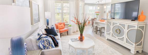 A living room with a grey couch, a white coffee table, and a television on a white cabinet.