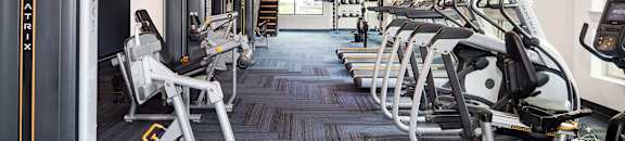 A gym with a variety of equipment including treadmills, elliptical machines, and weight machines.