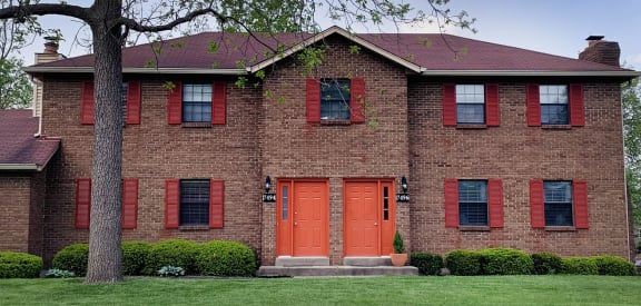 a brick house with red doors and a tree