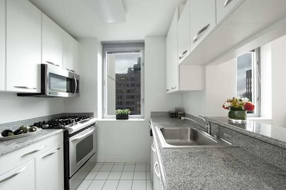 A modern kitchen with white cabinets and a grey countertop.at 'The Metropolis', New York