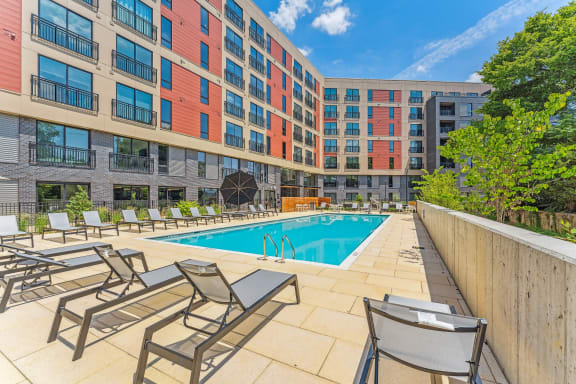 a swimming pool with chairs and a building in the background