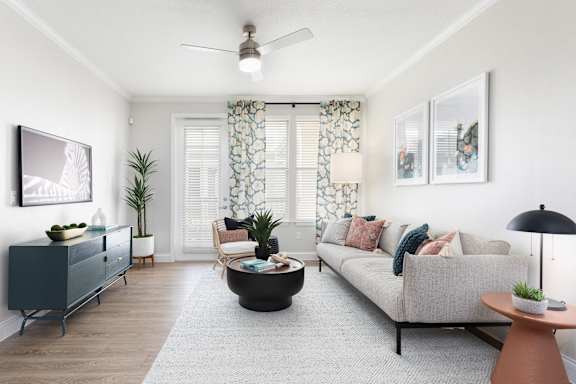 A living room with a grey couch, a black coffee table, a blue cabinet, a plant, a painting, a lamp, and a ceiling fan.