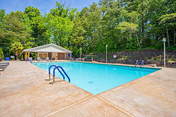A swimming pool surrounded by trees and a small building. at West Pointe Apartments, Apartments, Burlington, NC