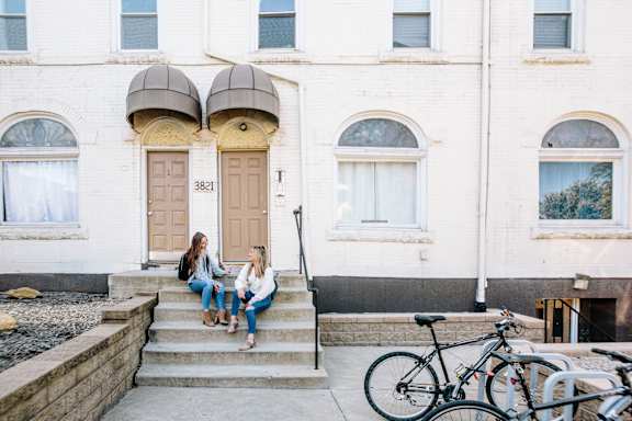 Two girls sitting on the steps of a building with a bicycle parked nearby.