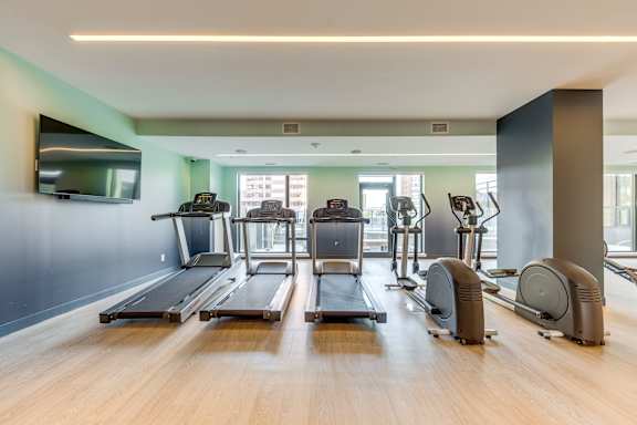 A gym with treadmills, elliptical machines, and a television.