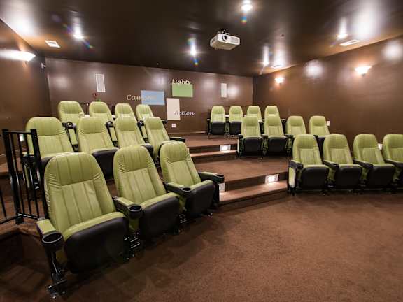 A row of green cinema seats are empty and facing a screen.