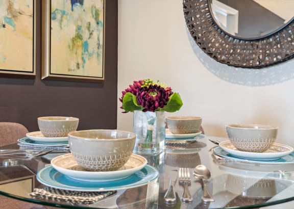 a glass dining table with plates and bowls and a vase with flowers
