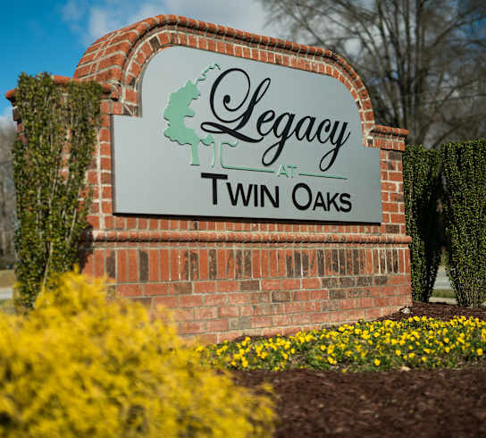 A sign that says Legacy Twin Oaks in front of some trees.