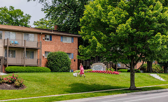 A woman in a pink dress is sitting on a lawn in front of a brick apartment building.