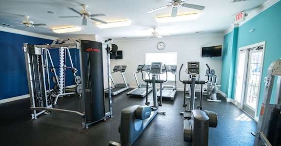 A gym with a variety of equipment including treadmills, weights, and a ceiling fan.